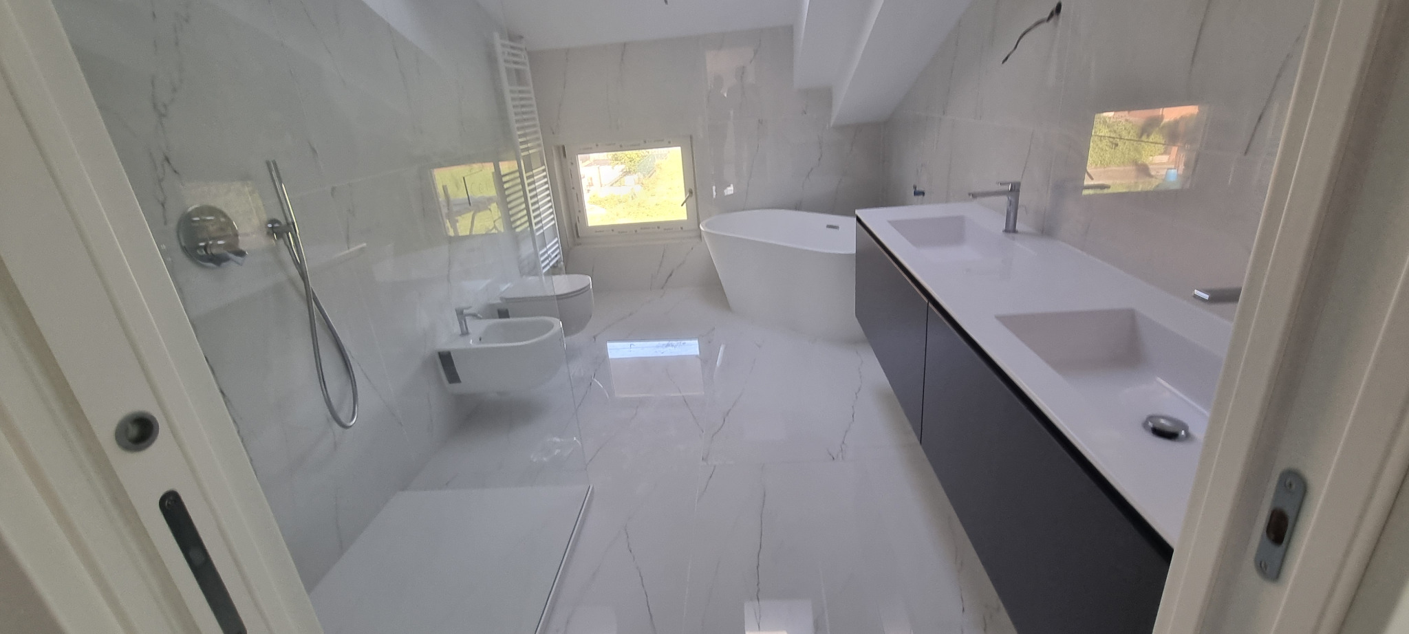 Bagno luminoso con rivestimento effetto marmo e vasca freestanding