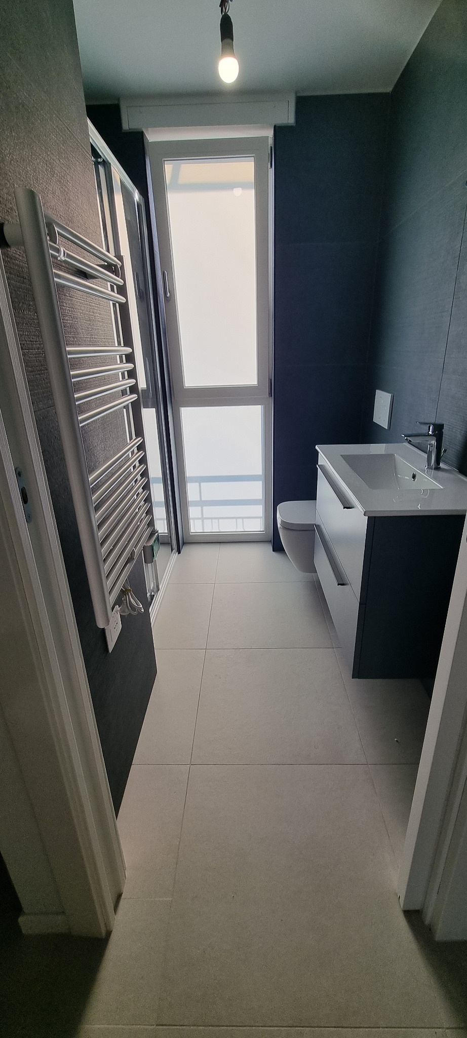 Bagno scuro con mobile sospeso e finestra verticale