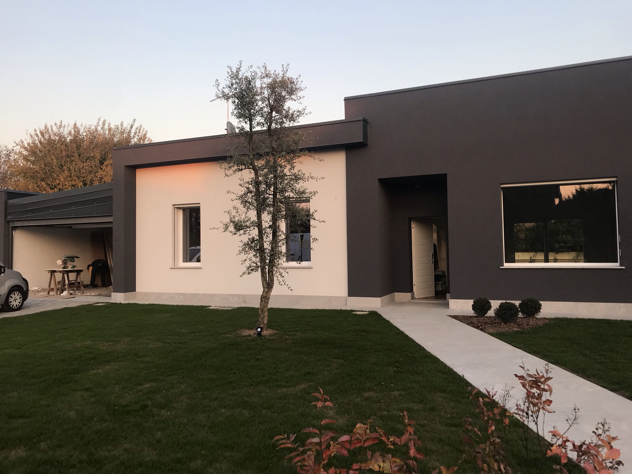 Fronte della casa con volumi chiari e scuri e percorso nel verde